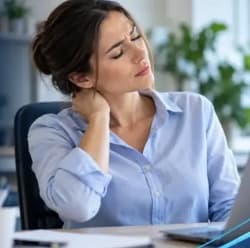 Woman at a desk holding the back of her neck in pain